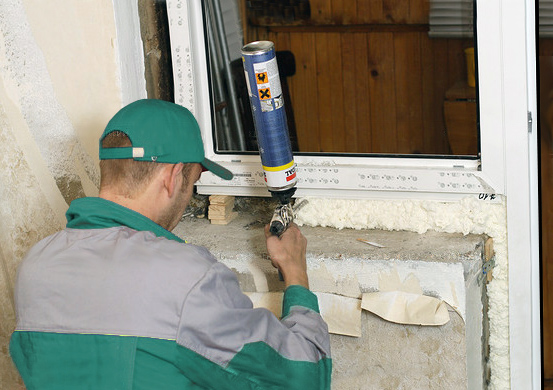 Монтажник заполняет пеной монтажный шов при установке ПВХ балконного блока